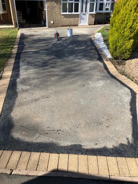 A partially finished driveway with a bordered edge and a bucket in the background.
